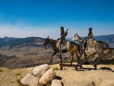 two statues of people riding horses on top of a rocky hill with mountains in the background