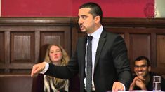 a man in a suit and tie giving a speech to people sitting at a table