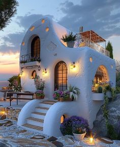 a white house sitting on top of a rocky hillside next to the ocean at dusk