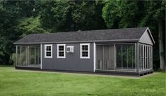 a gray and white shed sitting on top of a lush green field next to trees