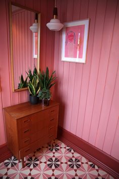 there is a plant on the dresser in this pink room with black and white floor tiles