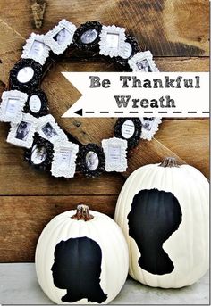 two white pumpkins sitting on top of a wooden table next to a black and white wreath