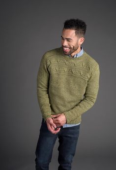 a man in a green sweater is smiling and looking at the camera while standing against a gray background