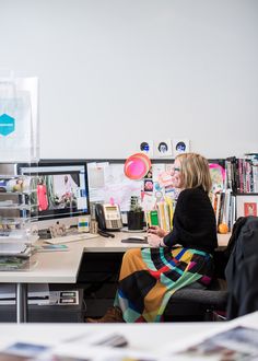 a woman sitting at a desk in front of two computer monitors and bookshelves