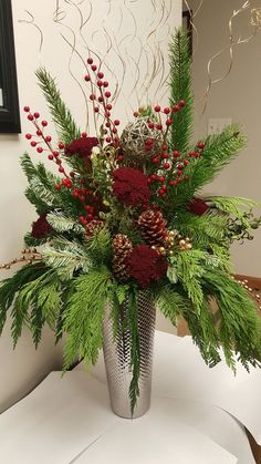 a silver vase filled with red flowers and greenery on top of a white table