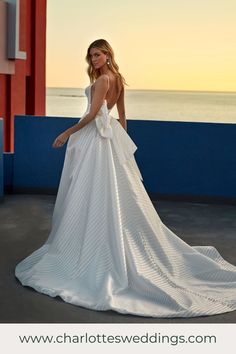 a woman in a white wedding dress standing on a balcony next to the ocean at sunset