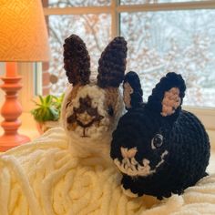 two crocheted stuffed animals sitting next to each other on a blanket in front of a window