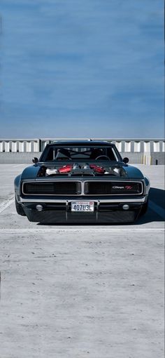 a black muscle car parked in a parking lot next to a white fence and blue sky