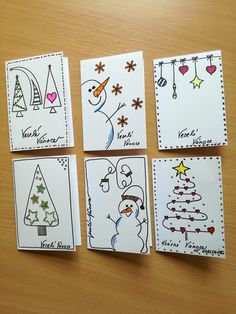 four christmas cards are arranged on a wooden table with white envelopes and black ink