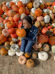 a woman sitting on the ground surrounded by pumpkins