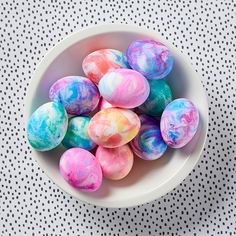 a white bowl filled with dyed eggs on top of a polka dot tablecloth surface