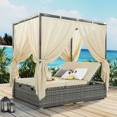 an outdoor bed with drapes and pillows on the deck next to the ocean,