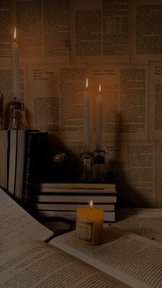 an open book sitting on top of a table next to a lit candle and books