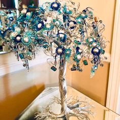 a silver tree with blue and white beads on it sitting on a table in front of a mirror