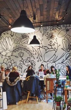 a group of people sitting around a table in front of a wall with flowers on it