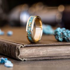 a wedding band with blue and gold glitter inlays sits on top of an open book