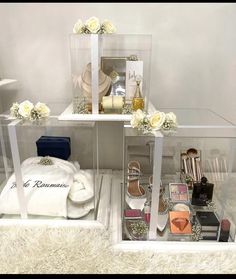 three clear boxes with white flowers and personal items in them sitting on a fur rug