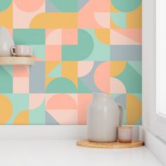 a white vase sitting on top of a counter next to a wall covered in colorful circles