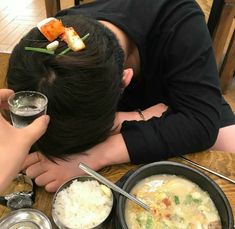 a man with his head on the table next to bowls of food and chopsticks