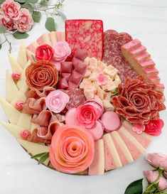 a platter filled with lots of different types of cheese and meats next to flowers