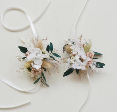 two bridal bouquets with white flowers and greenery tied to each other on a table