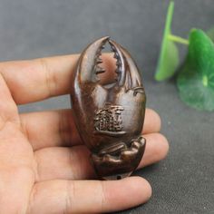 a hand holding a small carved figurine in it's right hand and another plant next to it