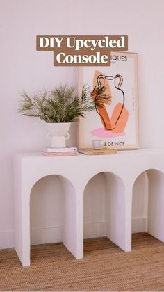 a white table topped with a potted plant next to a painting on the wall