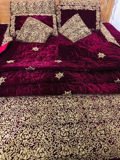 the bed is made with red velvet and gold embroidered bedspread, along with matching throw pillows