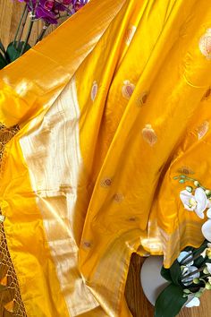 This exquisite handwoven banarasi silk saree in mango yellow color with minakari anar buttis is nothing but enchanting. Beautiful border with tine beaded lines and traditional motifs accentuates the saree very well. The grand elaborate zari woven pallu is nothing but regal. Approximate Length 6.5 mtrs (inclusive of blouse length)Height - 46 - 52" Saree comes with fall, picot and tassels done. Blouse piece is cut. Approximate weight - 1.3 lbs Kindly Note : The colors you see on your device may vary due to the color reproduction, brightness and resolution of individual devices. If you'd like more clarity before your purchase, please contact our support team. Yellow Dola Silk Traditional Wear With Pallu, Orange Banarasi Silk Saree With Meenakari, Yellow Saree With Cutdana In Traditional Drape, Yellow Traditional Wear With Pallu In Dola Silk, Traditional Yellow Dola Silk Saree, Yellow Dola Silk Saree For Festivals, Gold Paithani Silk Traditional Wear For Eid, Yellow Dola Silk Dupatta With Cutdana, Orange Paithani Silk Dupatta With Zari Work