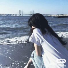 a woman sitting on top of a beach next to the ocean with her hair blowing in the wind