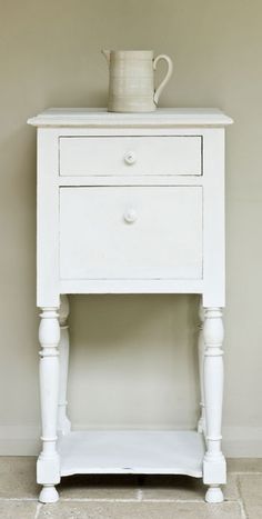 a white night stand with two drawers and a vase sitting on it's side