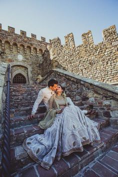 a man and woman sitting on the steps of an old castle with their arms around each other