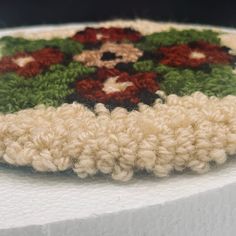 a close up of a crocheted doily on a white table cloth with red and green flowers