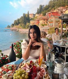 a woman sitting in front of a table full of food and drinks near the water