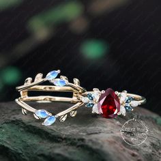 two gold rings with red and blue stones on top of each other, sitting on a rock