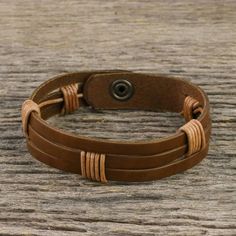 Chaloemphon of Thailand presents this men's leather wristband bracelet. The light brown leather has three horizontal slits. The artisan has wrapped two sections in black leather cord in artful intervals adding to the bracelet's texture and visual impact. The bracelet closes with a brass snap. Adjustable Leather Wristband With Waxed Finish, Adjustable Waxed Leather Bracelet, Brown Leather Wrap Bracelet For Gift, Brown Leather Wrap Bracelet Gift, Brown Leather Wrap Bracelet As Gift, Adjustable Rugged Leather Bracelet, Rustic Adjustable Leather Strap Bracelets, Adjustable Brown Leather Sweatband Wristband, Adjustable Brown Leather Wristband