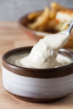 a spoon full of mayonnaise sitting in a bowl on top of a wooden table