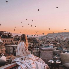 a woman sitting on top of a roof looking at hot air balloons in the sky