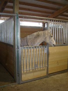 a white horse sticking its head over the top of a fenced in area with wood flooring