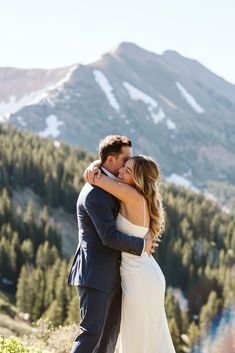 a bride and groom embracing each other in the mountains