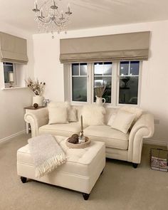 a living room filled with furniture and a chandelier hanging from the ceiling in front of two windows