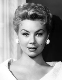 a black and white photo of a woman with big earrings on her head, looking at the camera