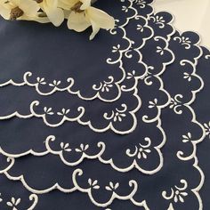 the table cloth has been embroidered with white thread and is next to some flowers on it