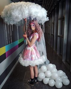 a woman in a pink and white dress holding an umbrella over her head while standing next to balloons