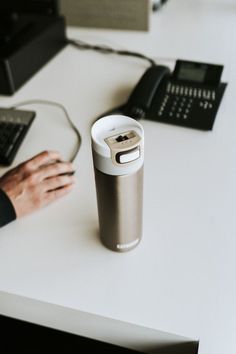 a person's hand resting on a coffee cup next to a computer mouse and keyboard