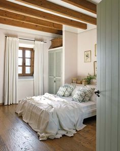 a white bed sitting in a bedroom next to a wooden floor covered in pillows and blankets