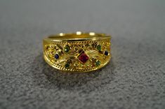 I am offering you this fabulous vintage  yellow gold tone wedding band stacker design ring. This piece is distinctive and stunning with the following features: It features 7 total combination round and square shaped oval cut bezel set emerald green, ruby and blue sapphire colored glass stones. These stones are set in a distinctive multi stone raised relief scrolled design setting. What a fantastic Etruscan style ring we have here. It is currently a size 8.  It measures app. 3/4 inch, by app. 1/2 Gold Ruby Ring With 17 Jewels For Wedding, Vintage Gold Stackable Rings For Formal Occasions, Gold Vintage Engraved Toe Ring, Vintage Gold Engraved Toe Ring, Gold Ruby Ring With Intricate Design For Anniversary, Anniversary Gold Ruby Ring With Intricate Design, Vintage Gold Toe Ring, Heirloom Gold Ruby Ring For Wedding, Gold Ruby Ring With Intricate Design For Wedding