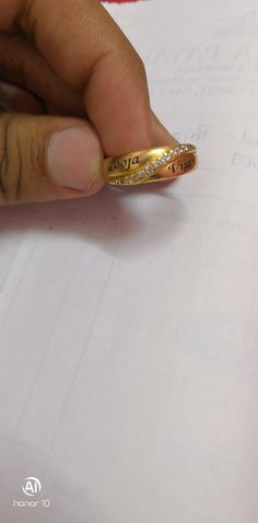 a person is writing on a piece of paper with a gold ring in their hand