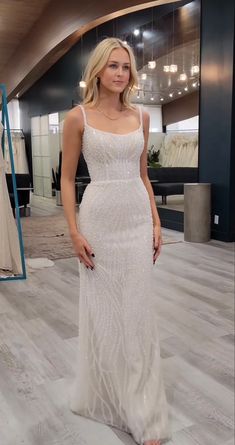 a woman standing in front of a mirror wearing a white dress with beading on it