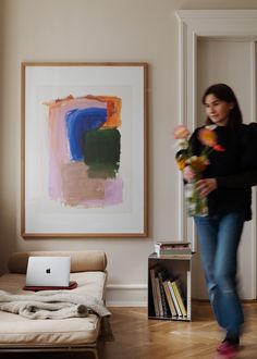 a woman walking through a living room with a laptop and flowers in front of her